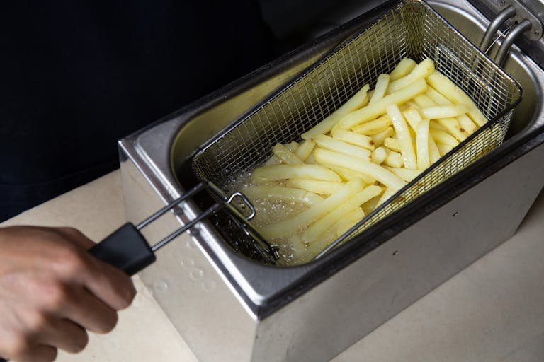 Close-up of french fries being deep-fried in a commercial fryer, hand holding the basket.